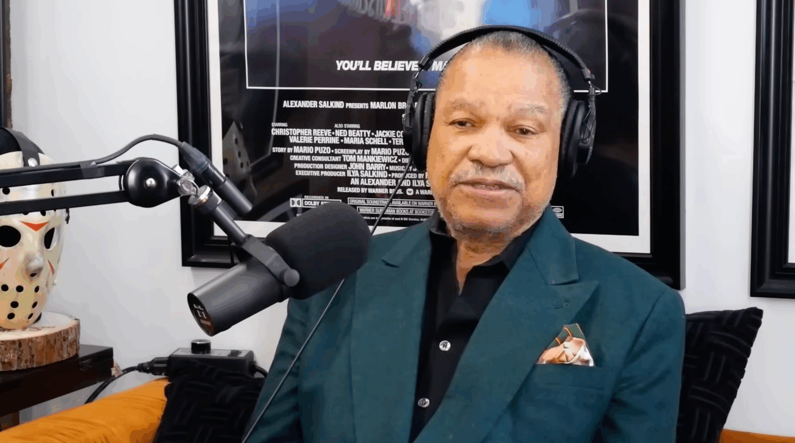 Billy Dee Williams in a blue blazer sitting at a microphone wearing headphones