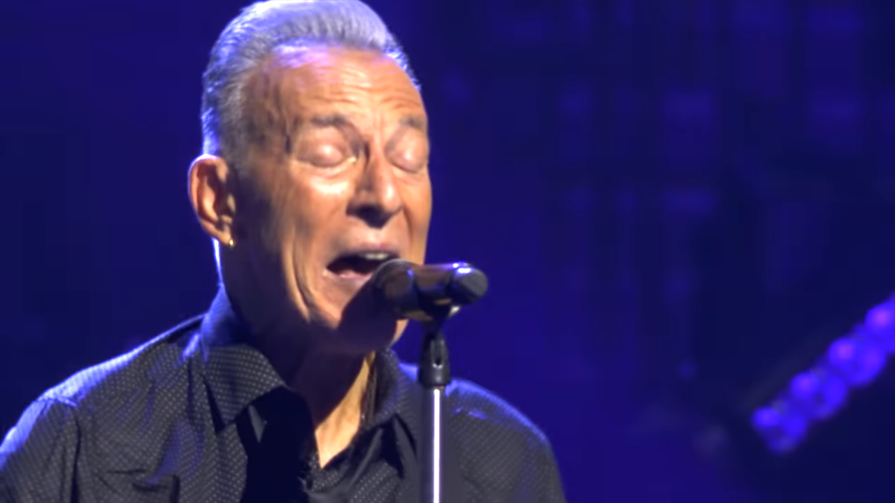 An older man, eyes closed, sings passionately into a microphone