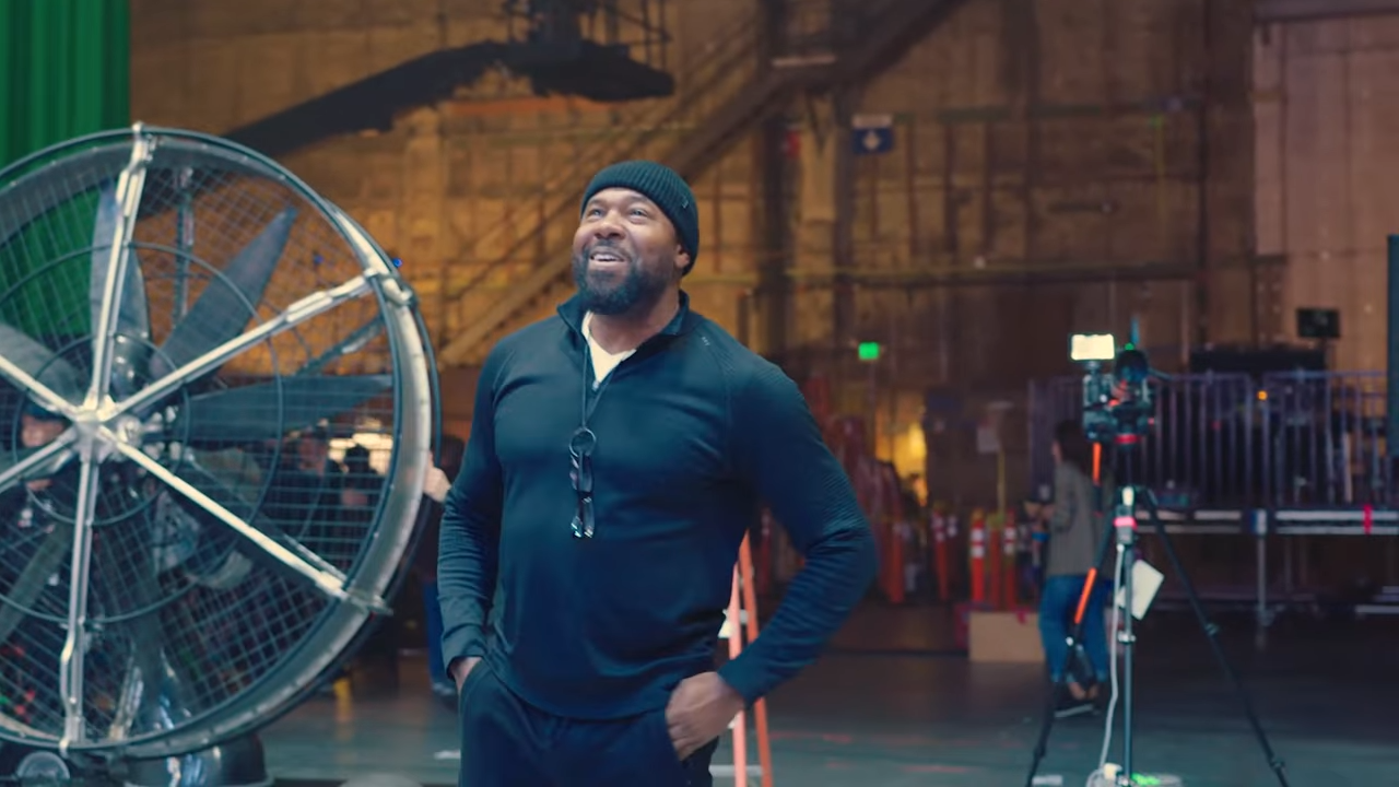 Director Antoine Fuqua stands on a soundstage, hands on hips, smiling