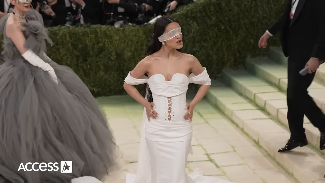 A young woman in a shoulderless dress and a blindfold poses at a formal event