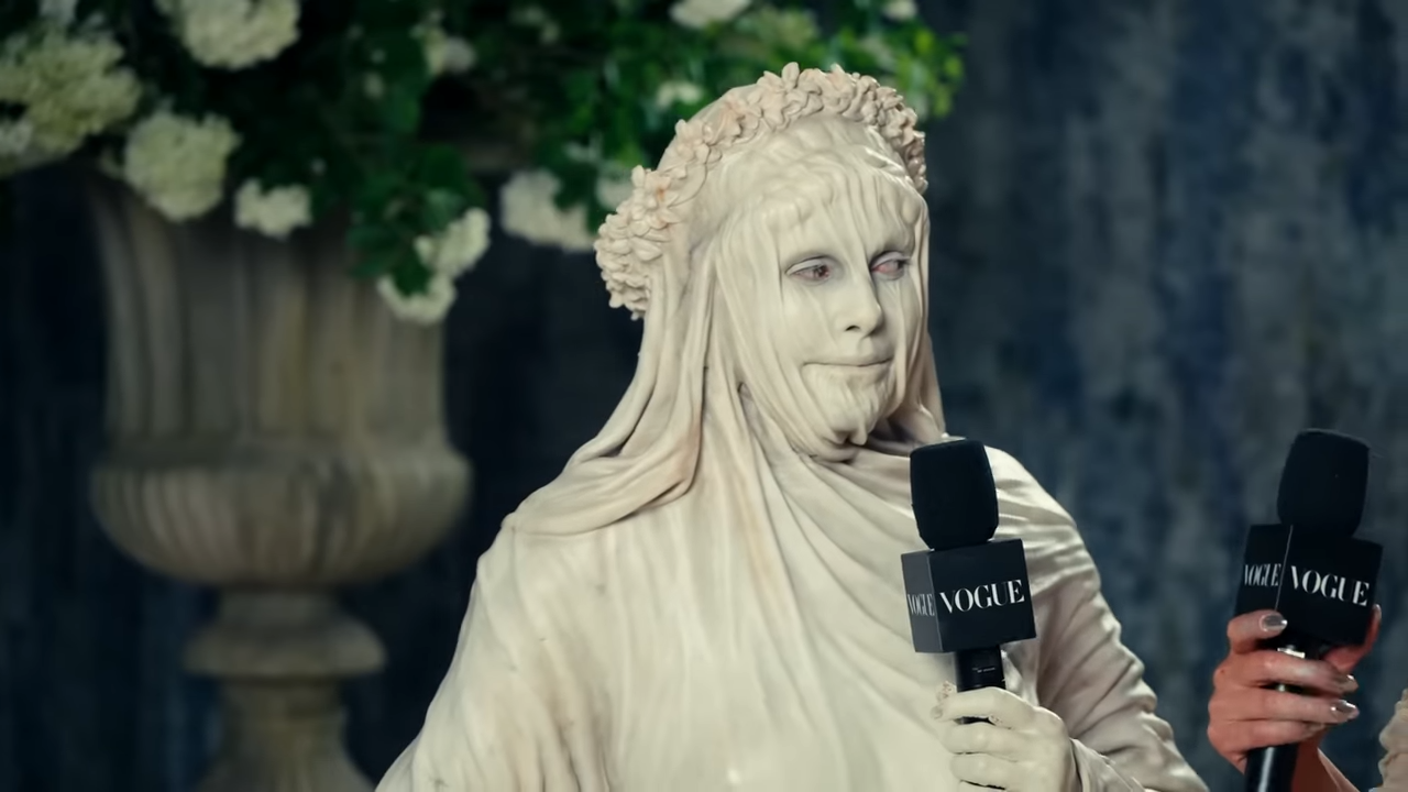 A woman in heavy makeup to resemble a statue holds a microphone