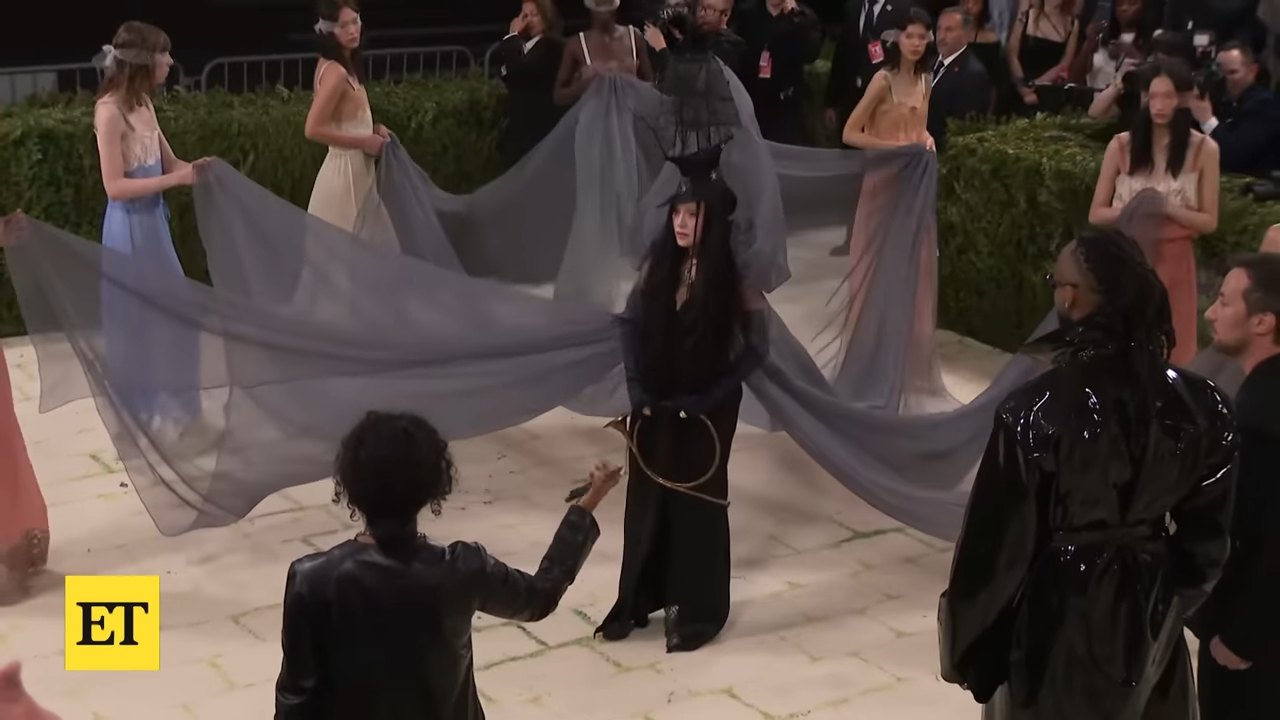 A woman covered head to toe in black stands surrounded by attendants at a formal event