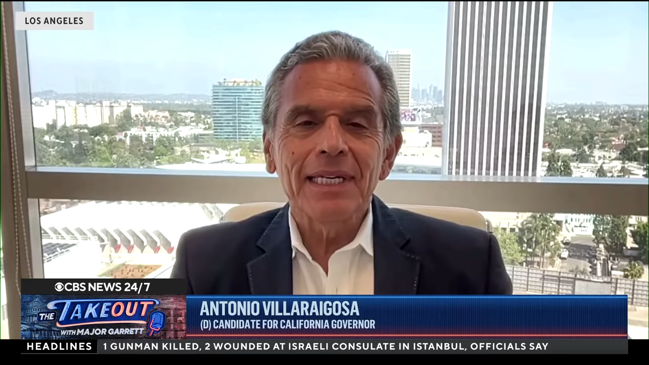 A man speaking on a TV interview with a daylight skyline in the background