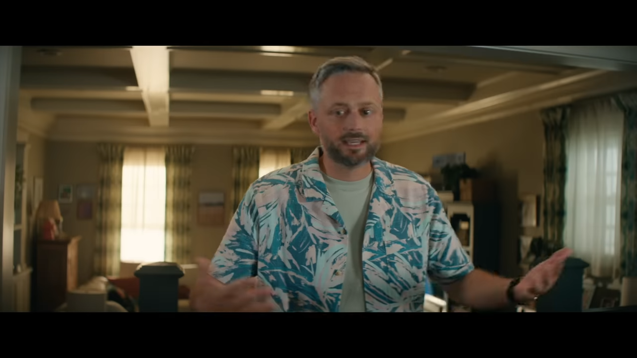 A dad stands in the living room of a modest suburban house giving instructions