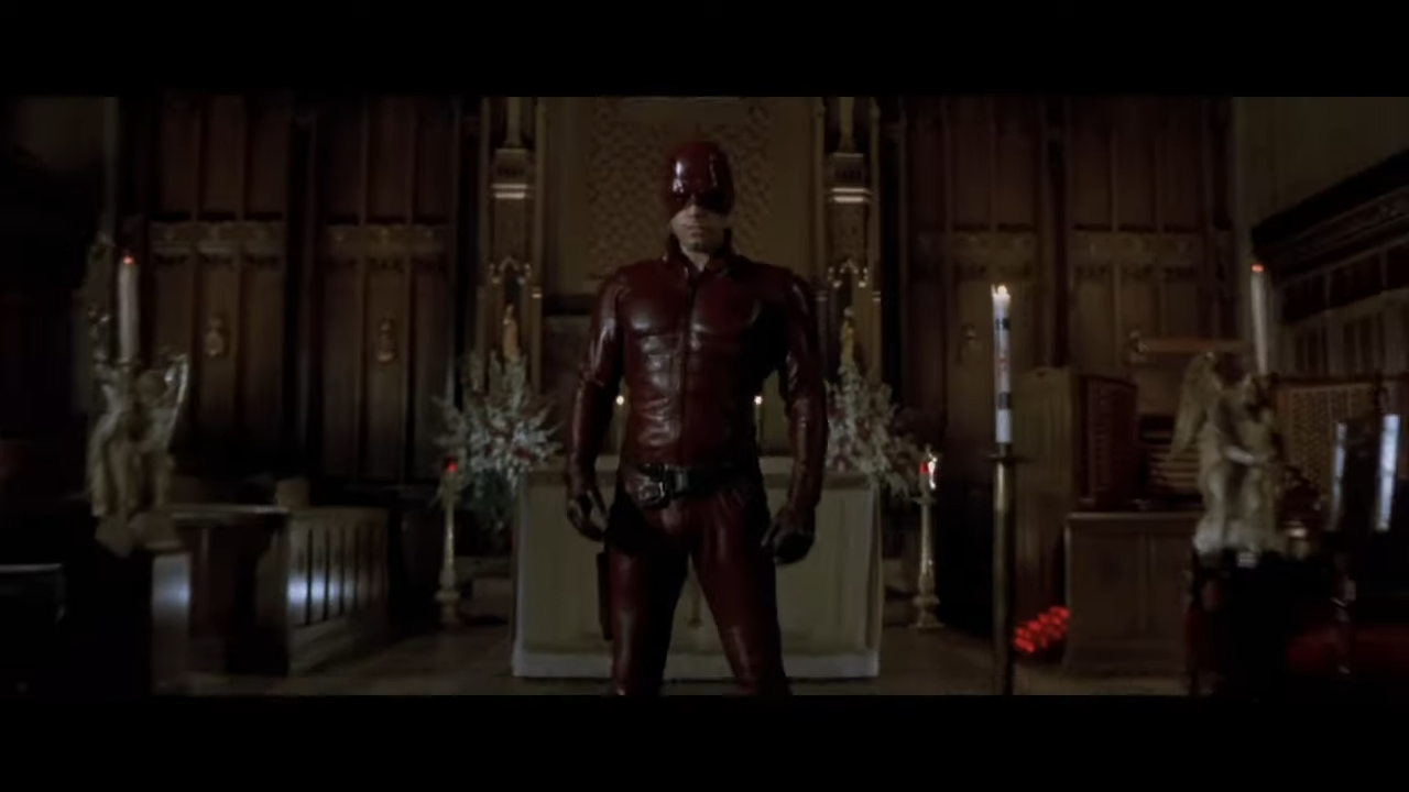 A leather-clad and masked superhero stands with his arms at his sides, threatening