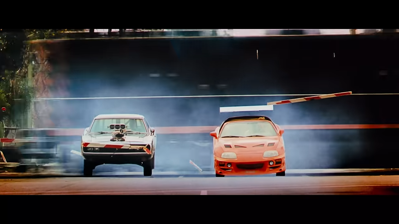 Two sports cars crash to the ground as a train speeds by behind them