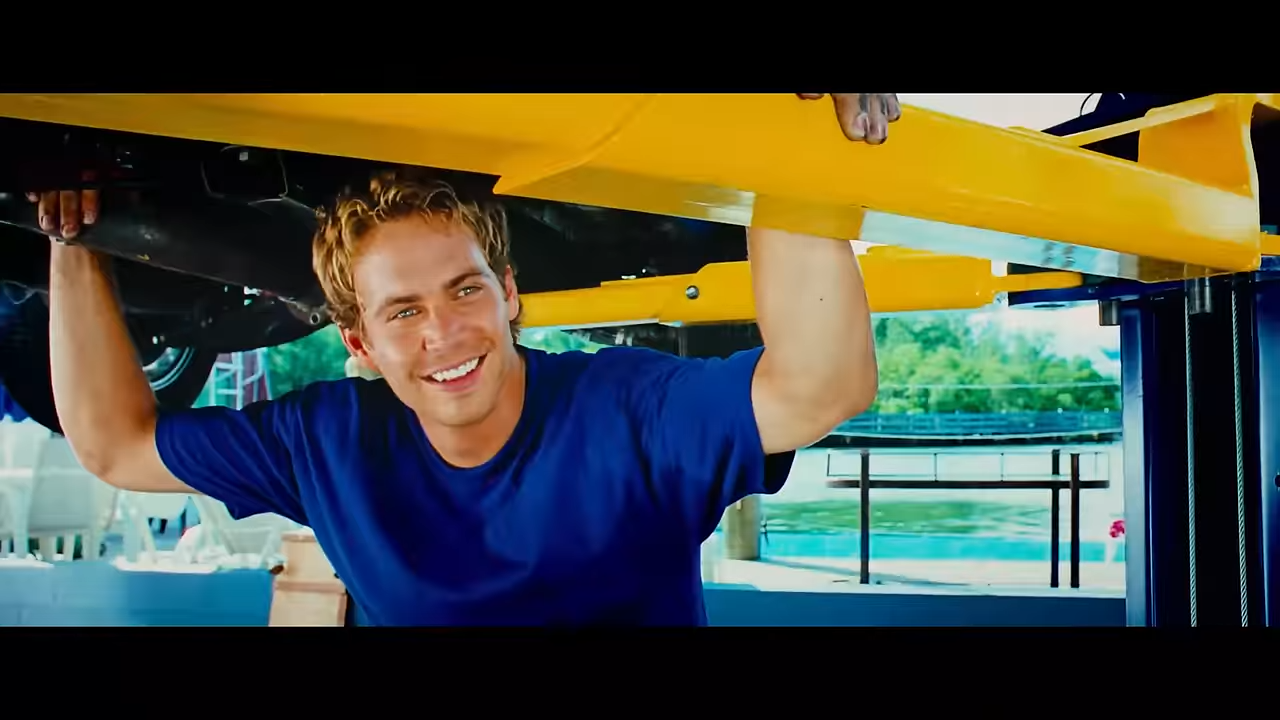 A young man smiles under a car on a lift