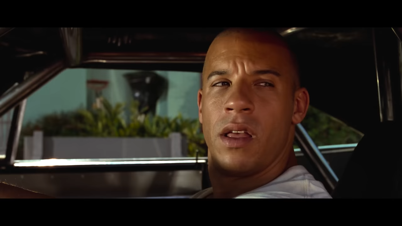A bald man scowls from the driver's seat of a car