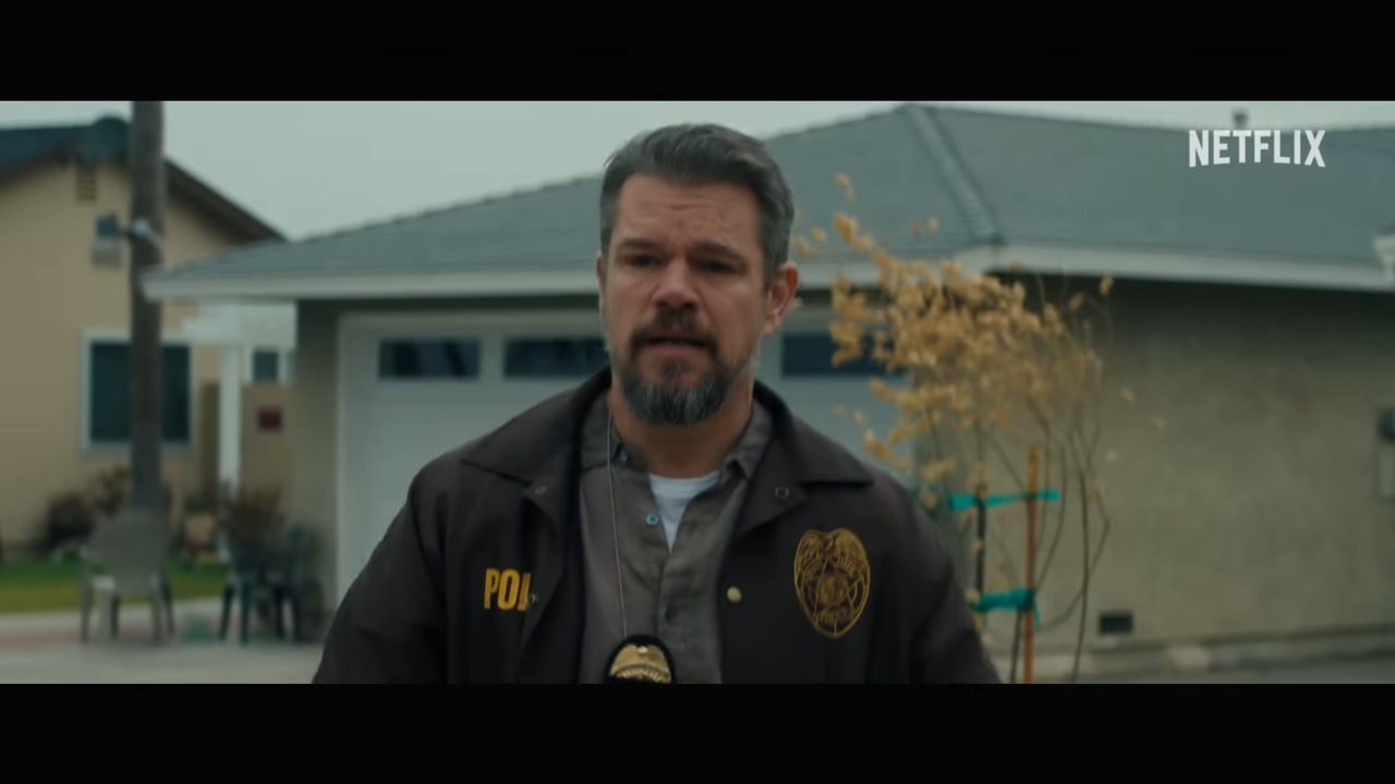 A man in police jacket walks through a suburban neighborhood