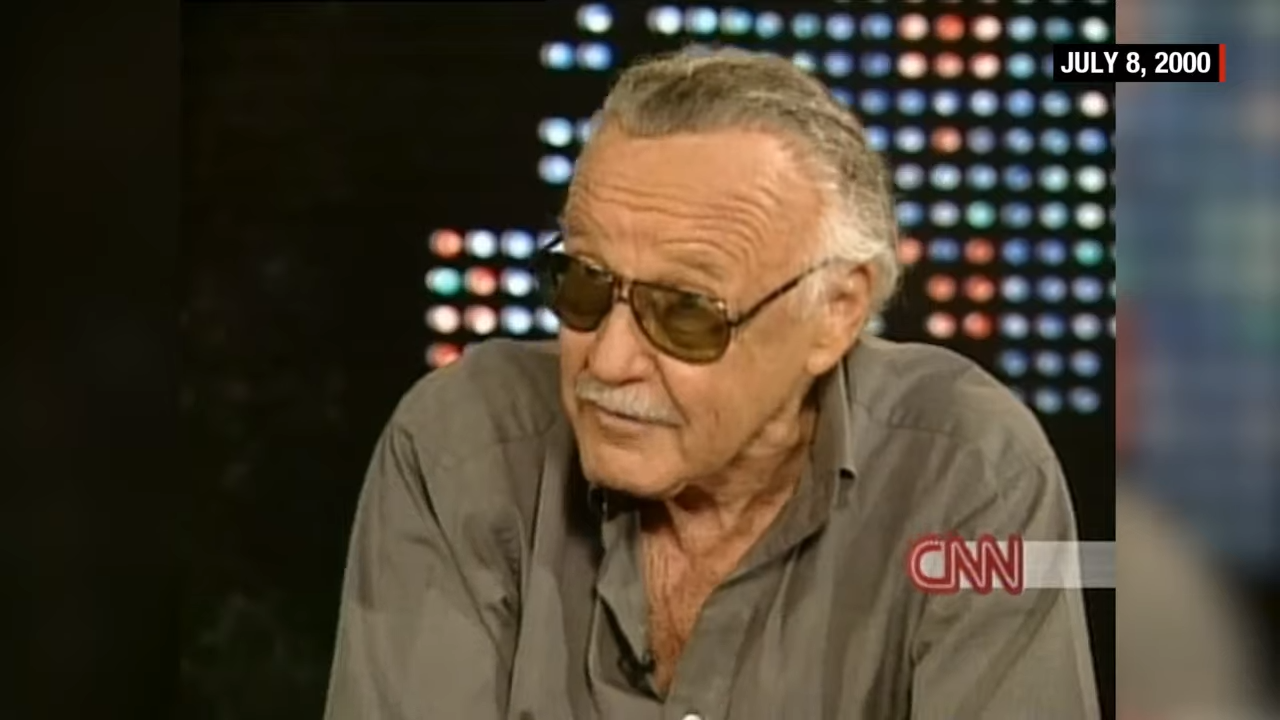 Stan Lee in sunglasses and an open-collared shirt during a TV interview