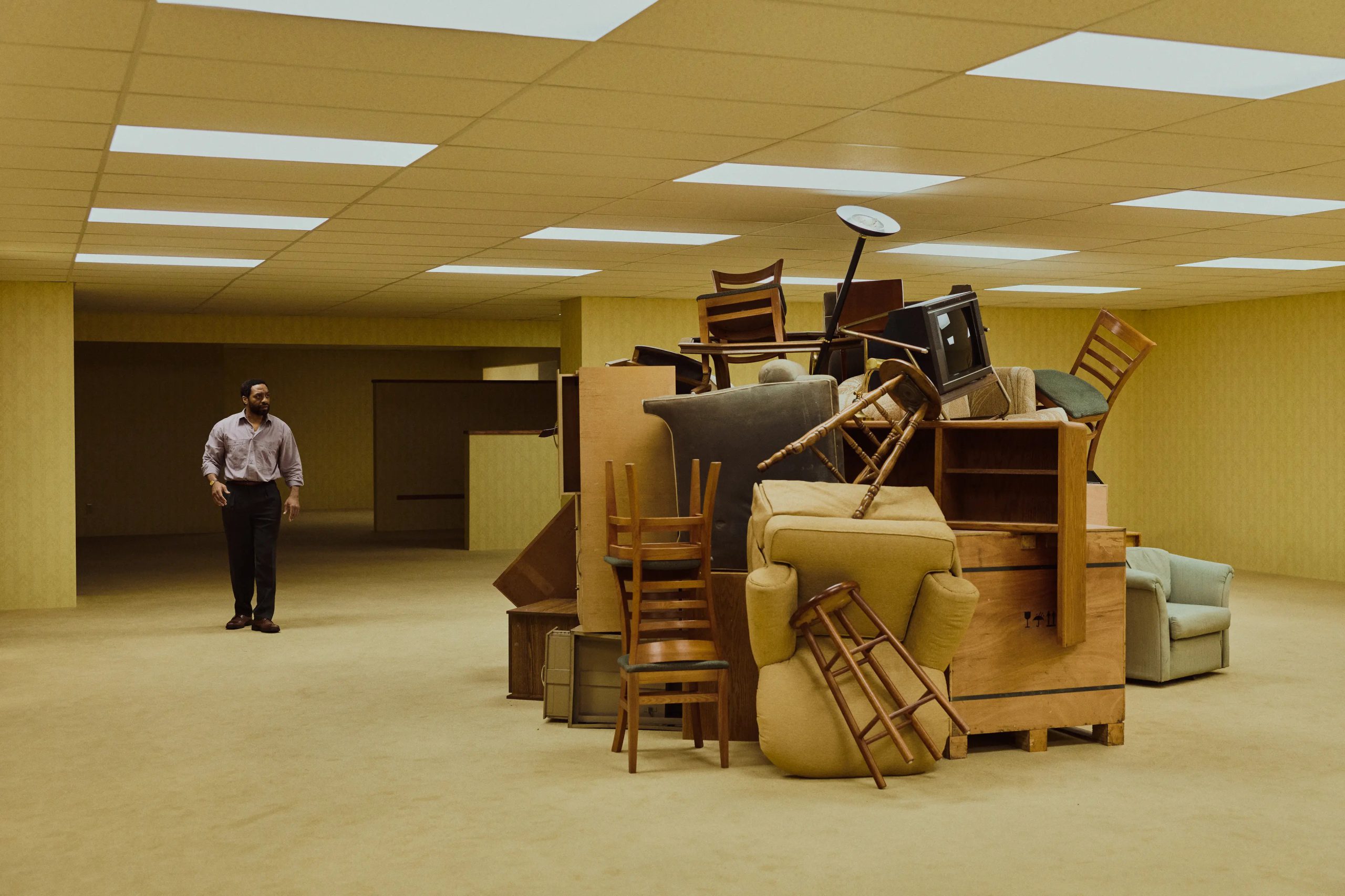 A man enters an office space where all the furniture is piled in the center of the room.