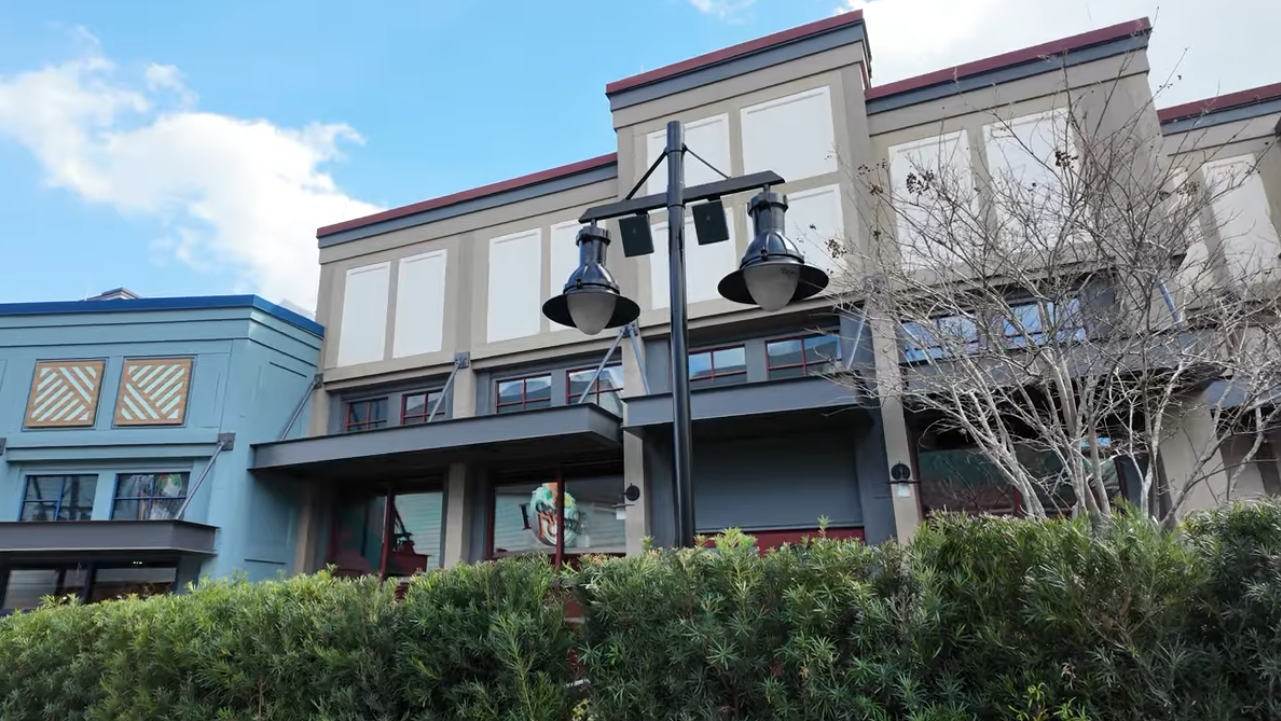 Storefront for Upcoming Six Ravens at Disney Springs, Brown and tan building without decor behind green hedge