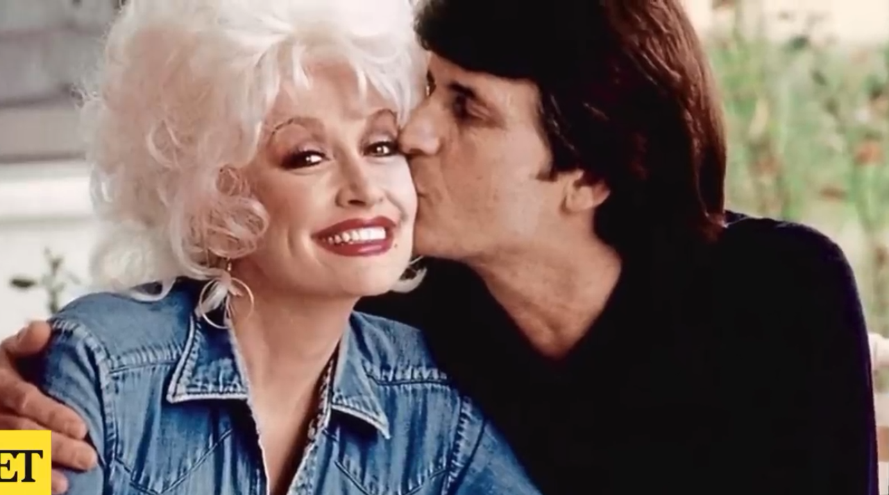 A Young Dolly Parton Smiles as Husband Carl Dean gives her a kiss on the cheeck