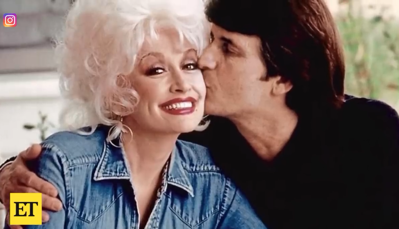 A young Dolly Parton smiling as Husband Carl Dean kisses her on the cheek
