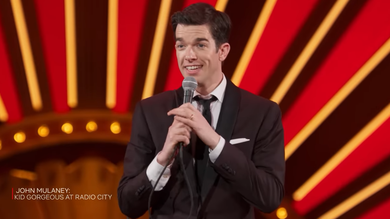 John Mulaney on stage in a suit and tie