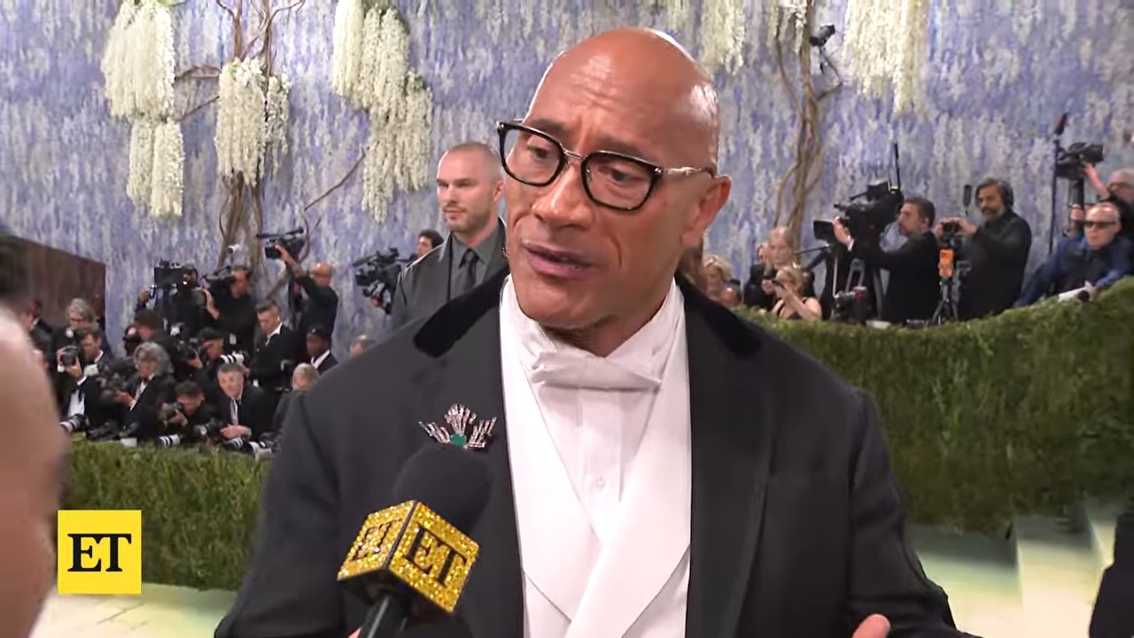 A bald man in formalwear speaks into a microphone
