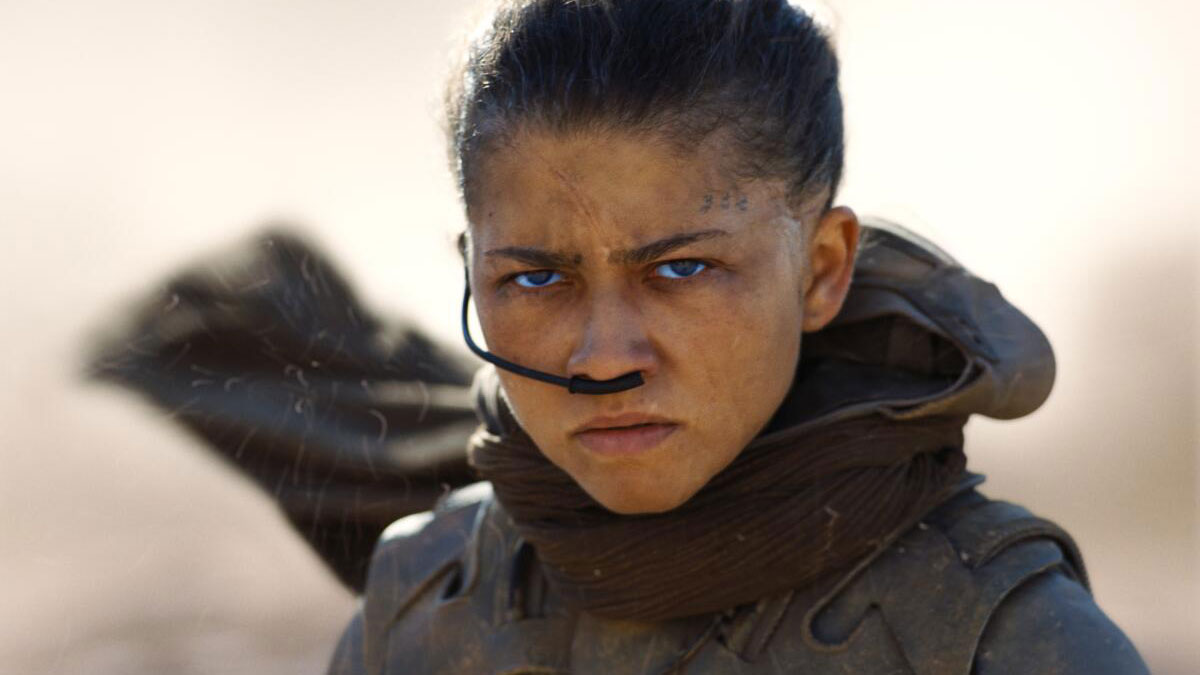 A young woman stands in a desert, expressing determination or resentment
