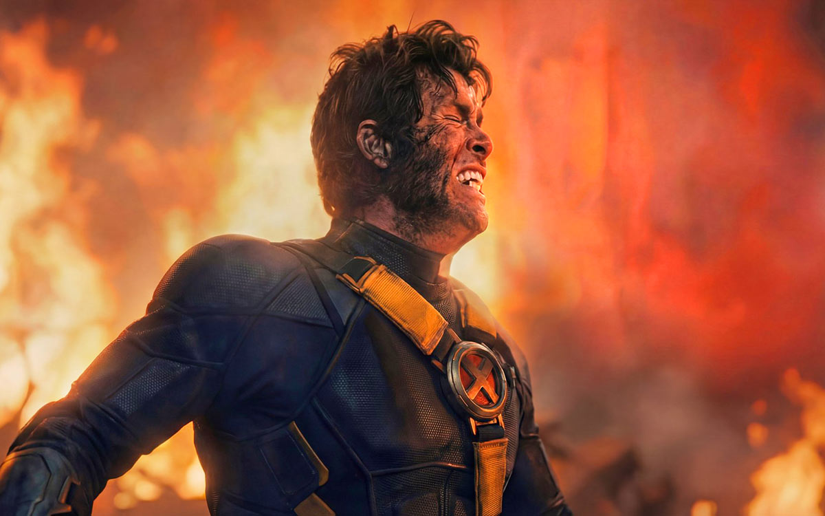 A man stands in front of flames, eyes closed and teeth clenched in pain