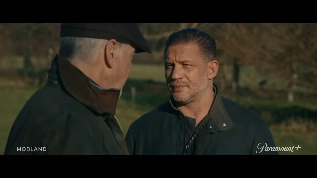 Two men face each other outdoors, seeming to have come to an understanding