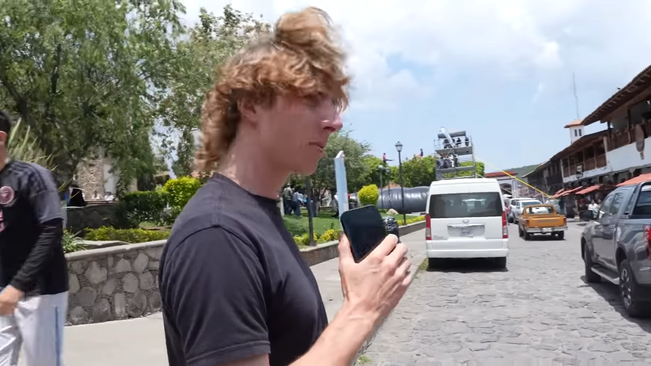 Reckless Ben on a street, holding his phone while the wind blows his hair over his face