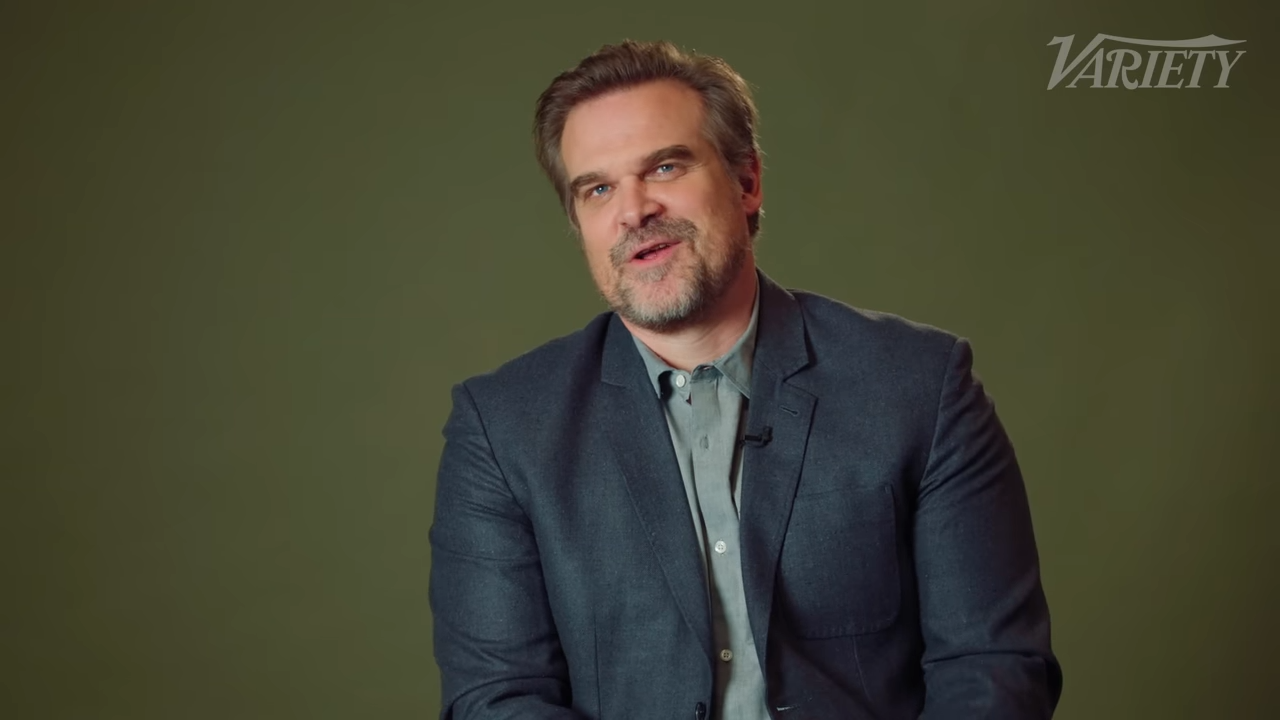 David Harbour in a sport jacket smiles and looks reflective