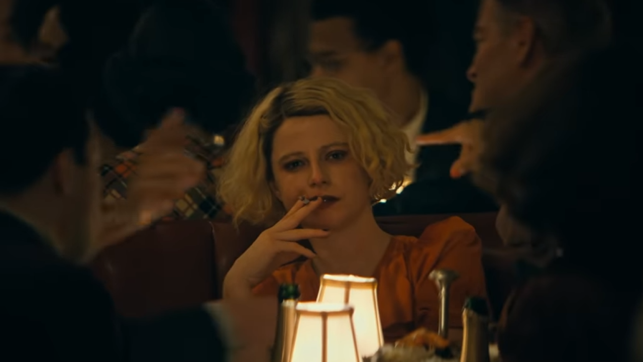 A woman sits in a lantern-lit bar smoking a cigarette with a smile