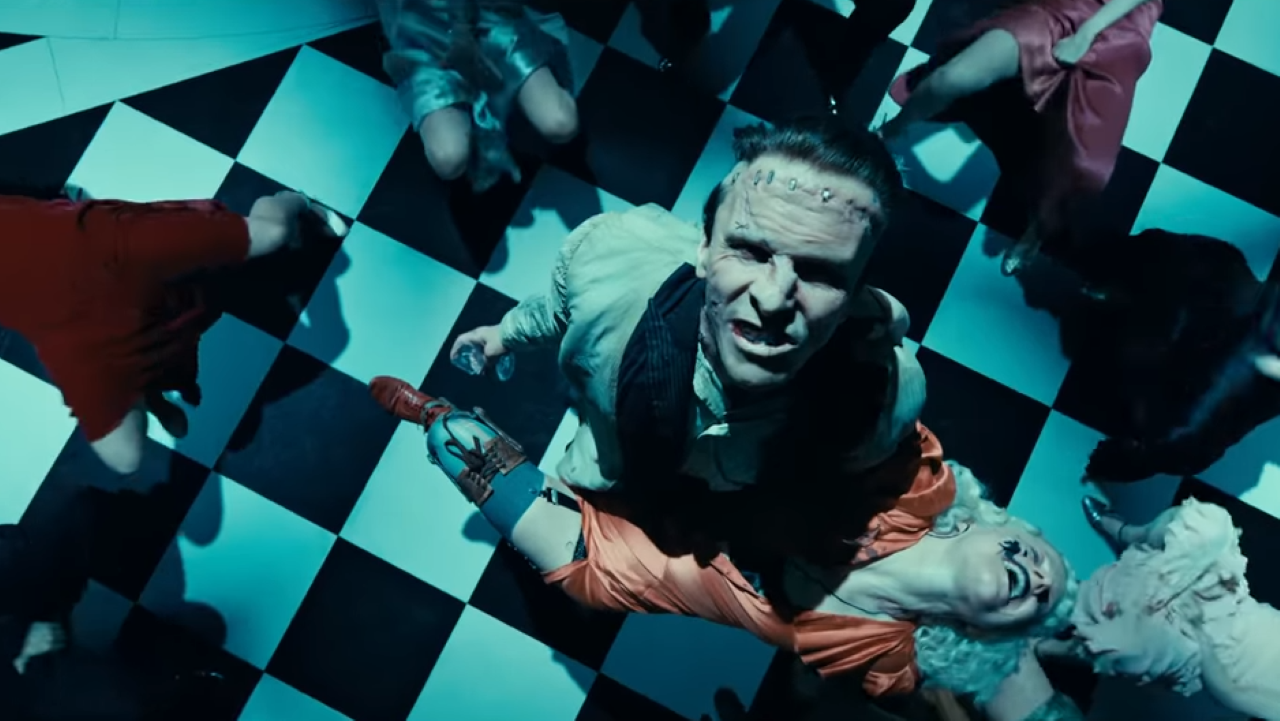 We look down on a man facing upward, with a sneer on his face as bodies lay around him
