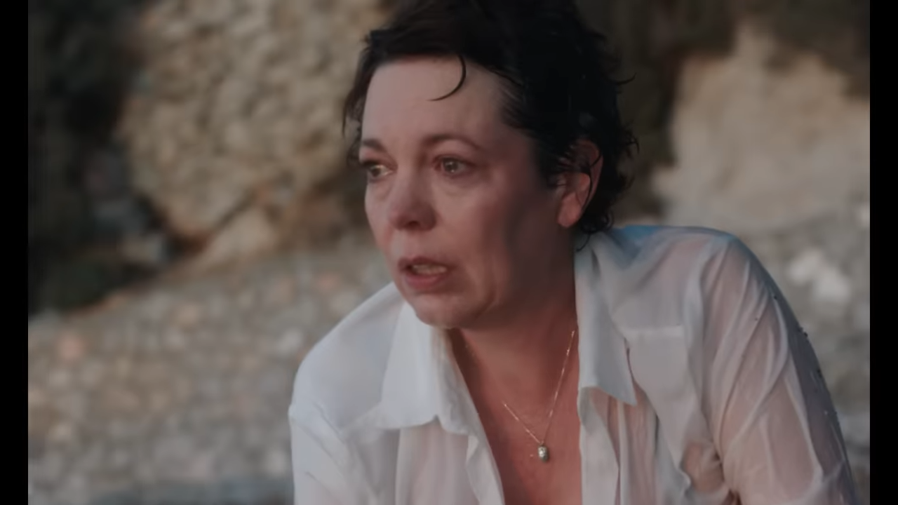 A soaked woman sits on a beach appearing distressed