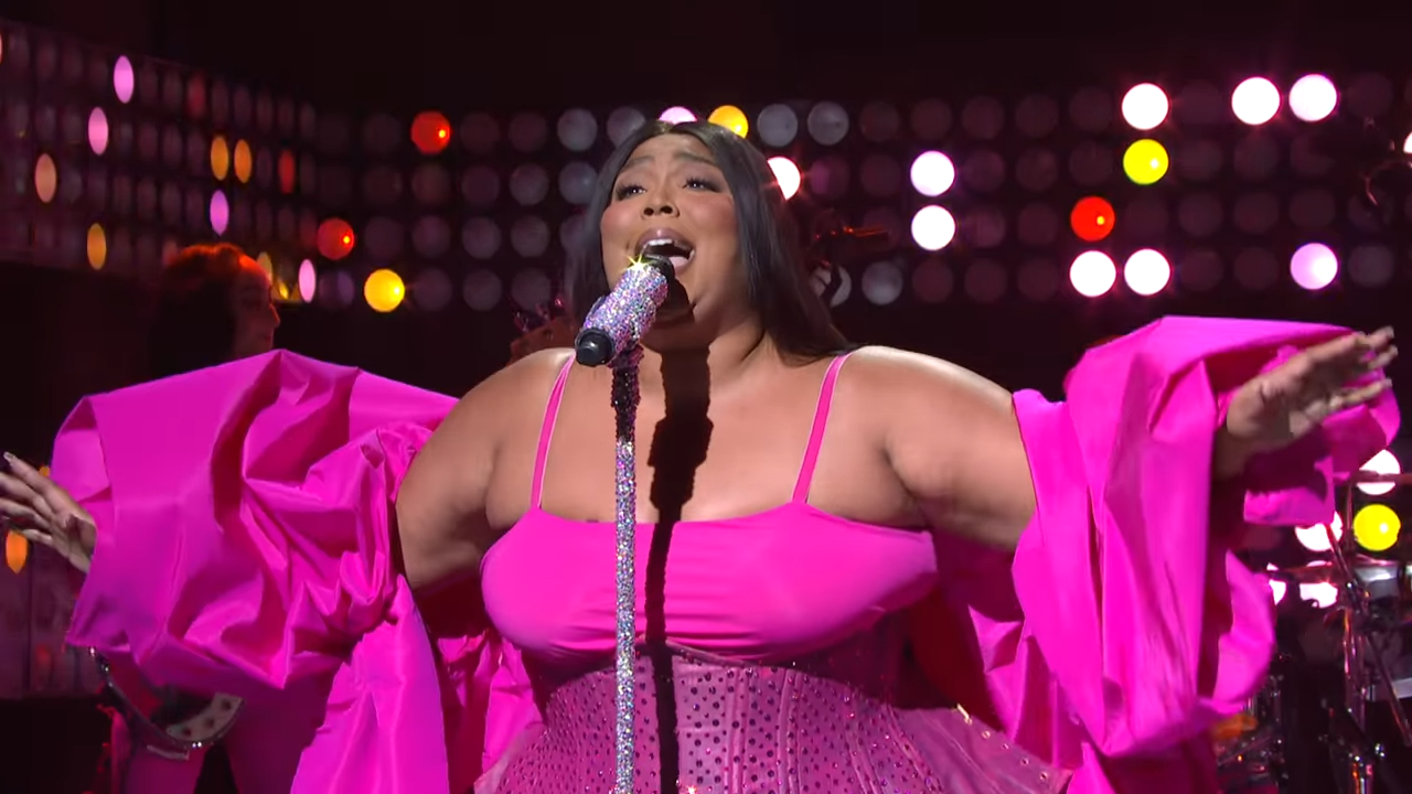 A singing woman in a billowing dress spreads her arms wide.