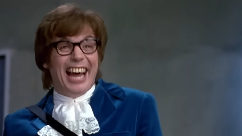 A man in a 60s style suit and glasses gives a toothy grin