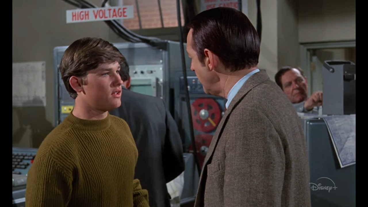 A young man talks to an older man in a 1960s computer lab