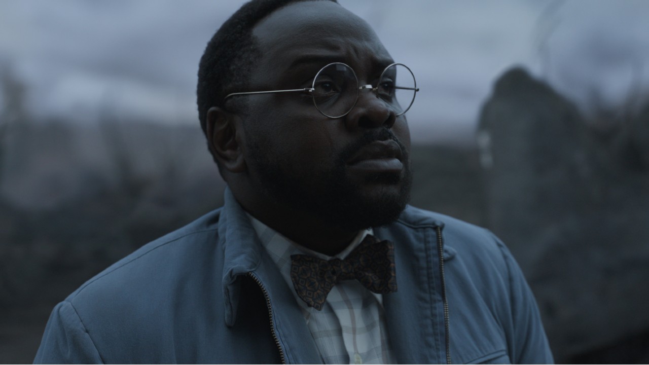 A black man wearing glasses and a bowtie looks upward