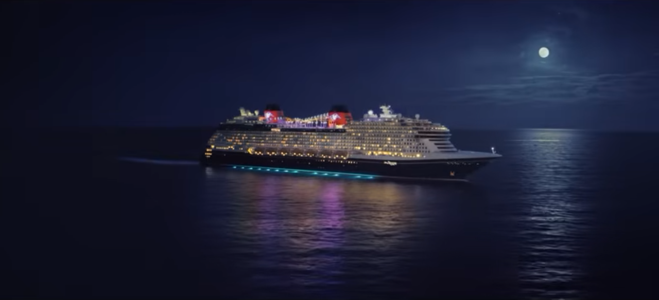 Picture of a cruise liner at night with the reflection of the moon and lights of the ship against the water
