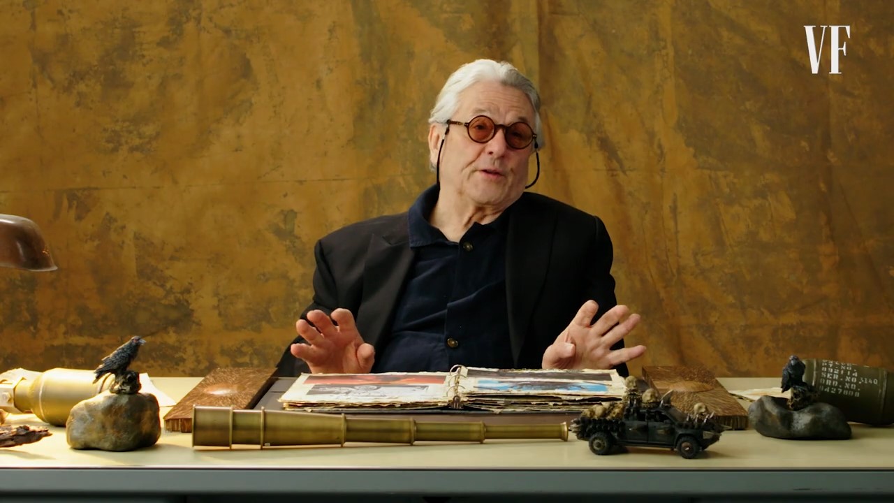 A man with white hair and red sunglasses gestures expressively 