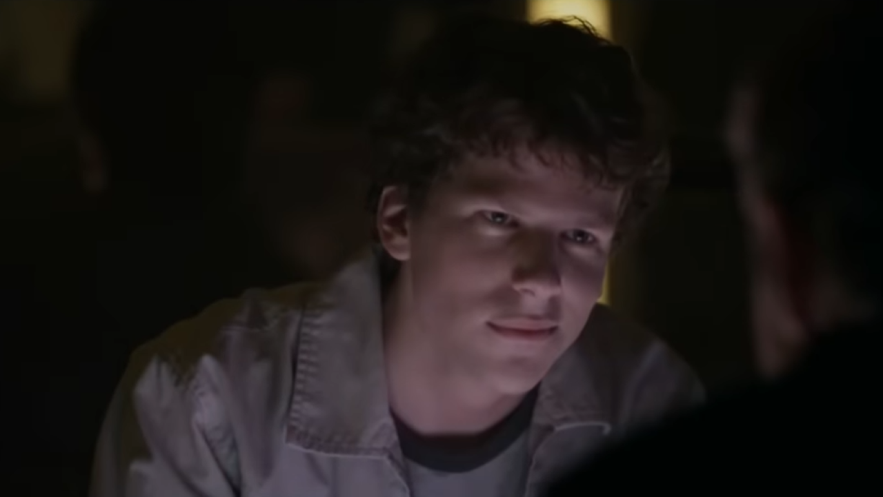 Jesse Eisenberg Social Network A young man in shadows smiles, appearing self-satisfied