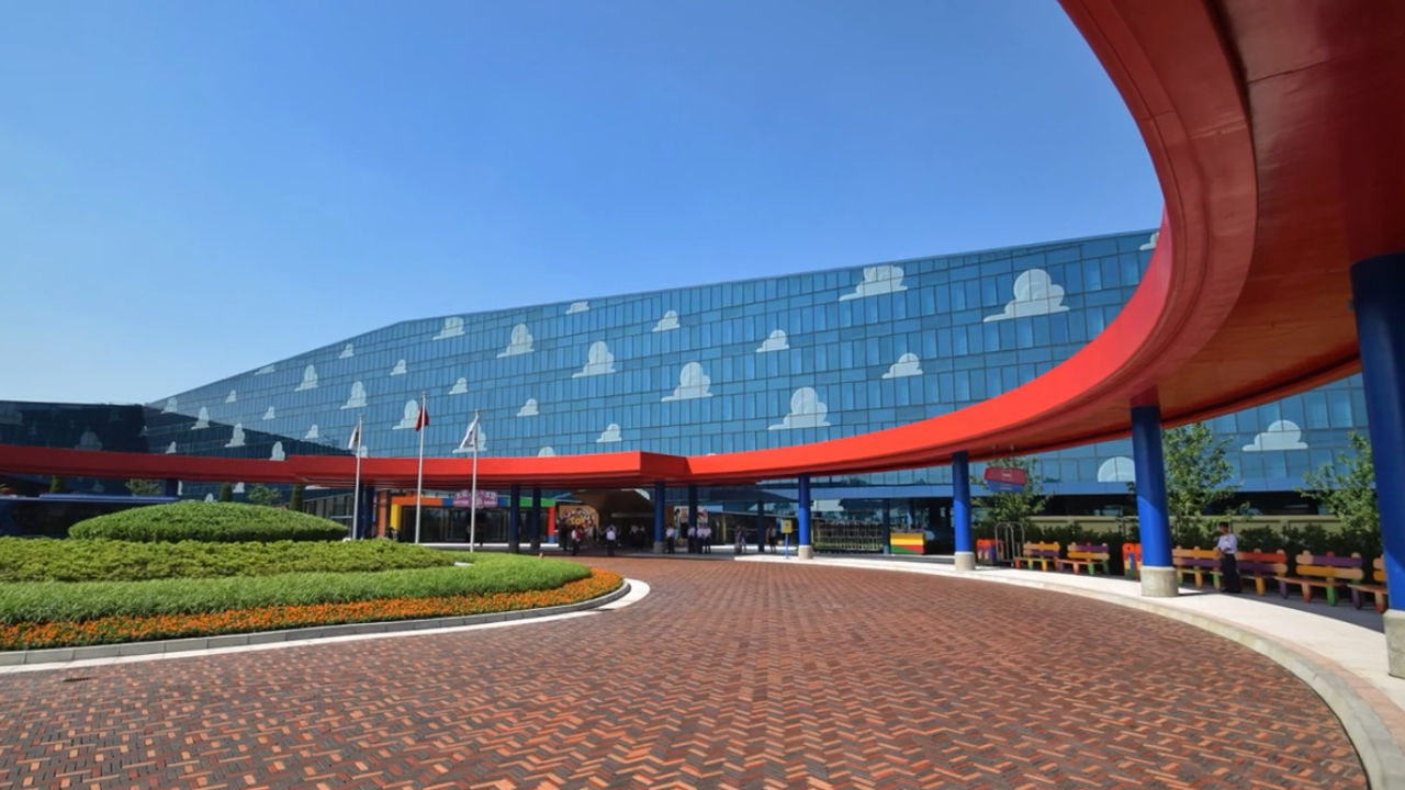Large, modern hotel with blue-tinted windows covered in painted clouds, and red covering stretching the length of the sidewalk