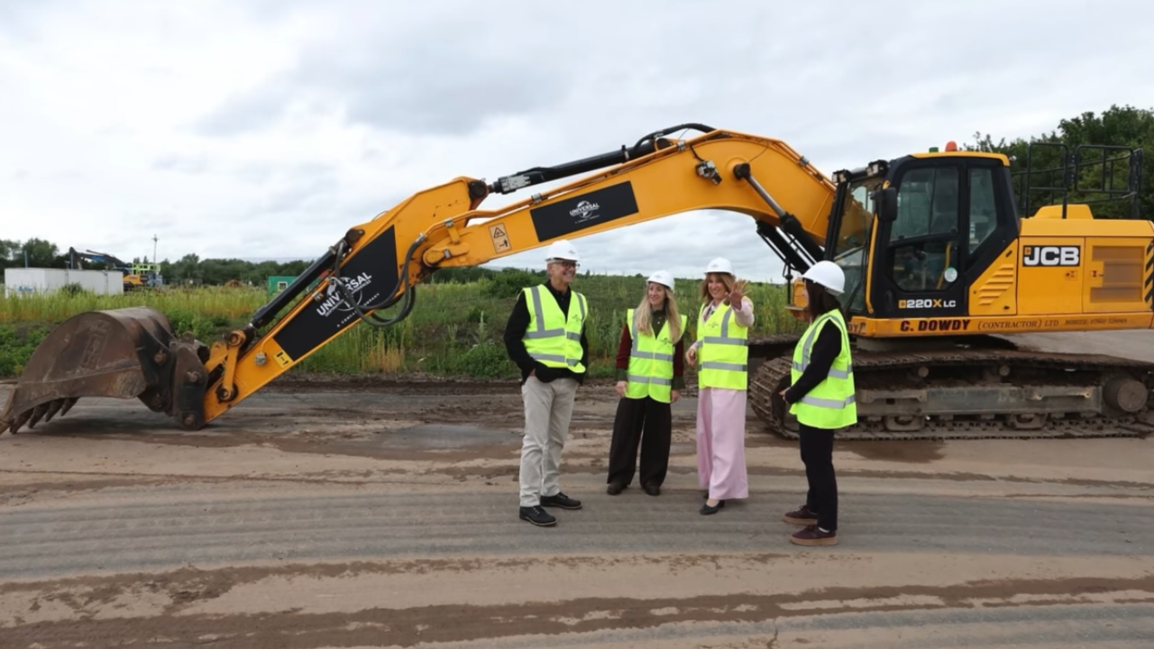 Excavator on flat dirt with four construction workers