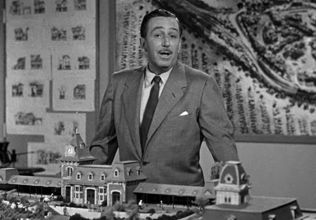 Black-and-white photo of Walt Disney standing behind a model of part of Disneyland
