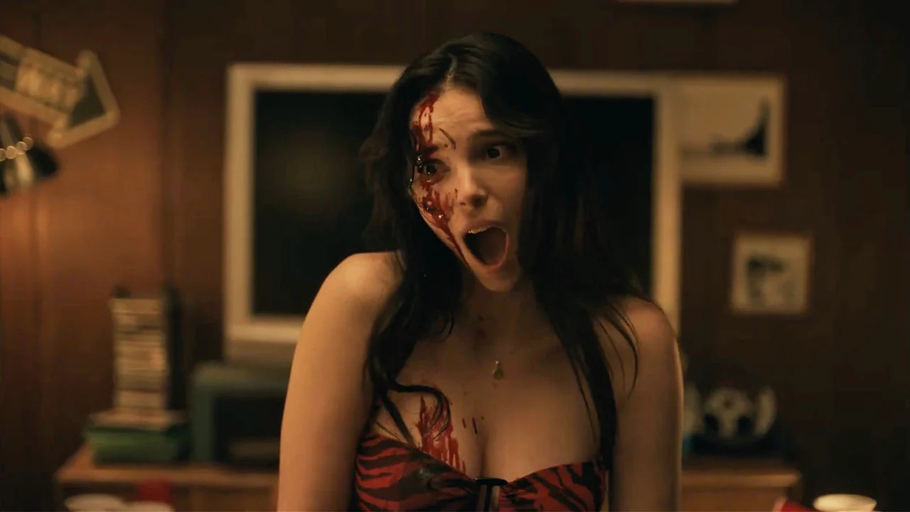 A young woman with blood on her face opens her mouth unnaturally wide
