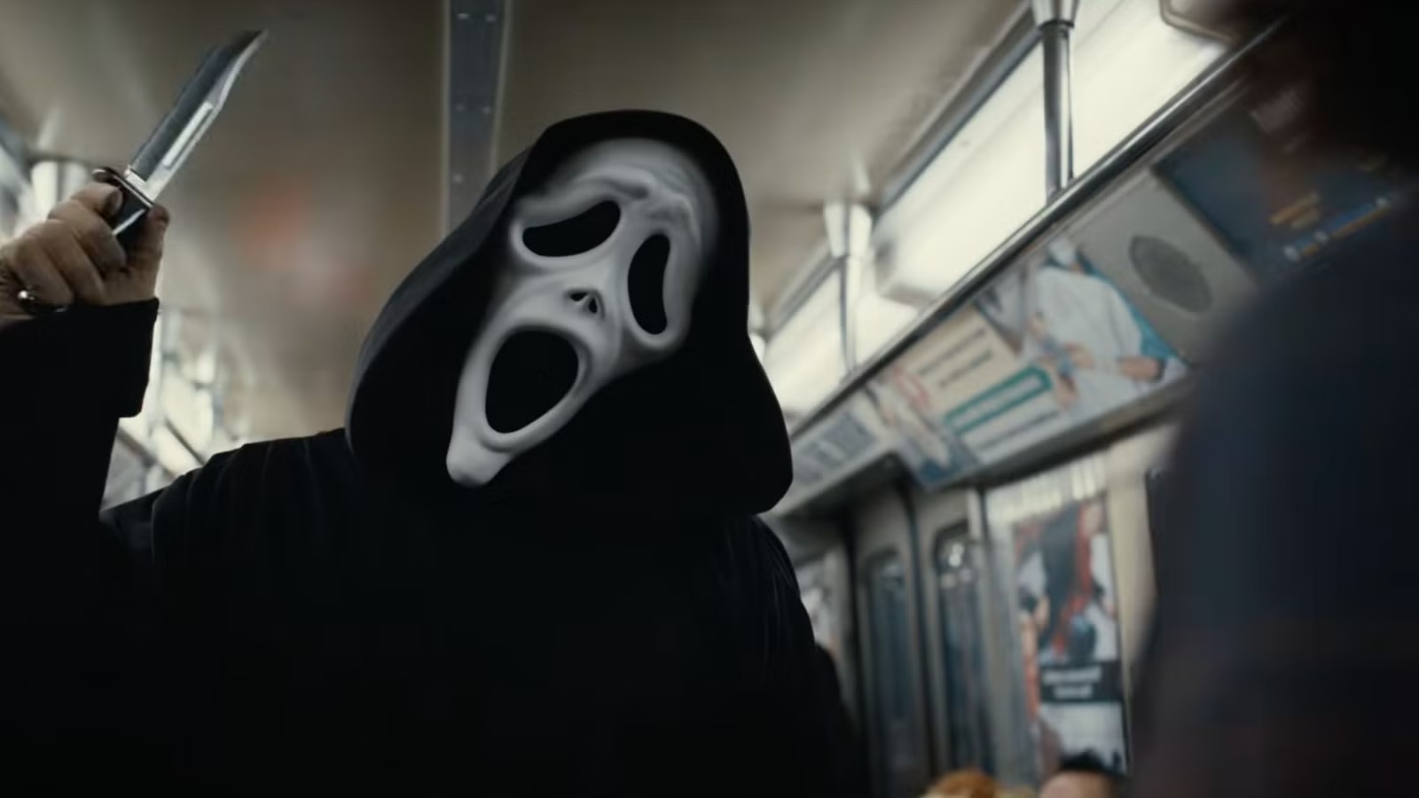 The Ghostface killer holds a knife in a subway car