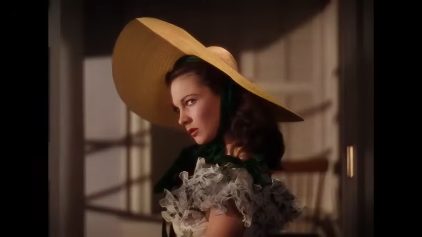 A woman in a wide-brimmed straw hat glares over her shoulder