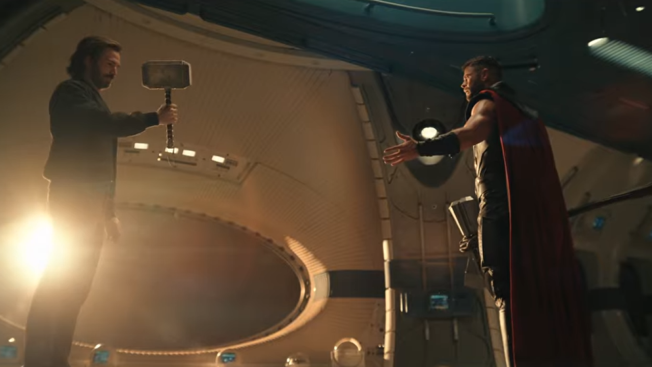 Steve Rogers holds Thor's hammer as Thor looks on