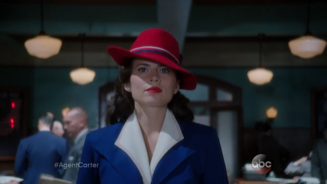 A confident woman in a wide-brimmed hat walks through an office
