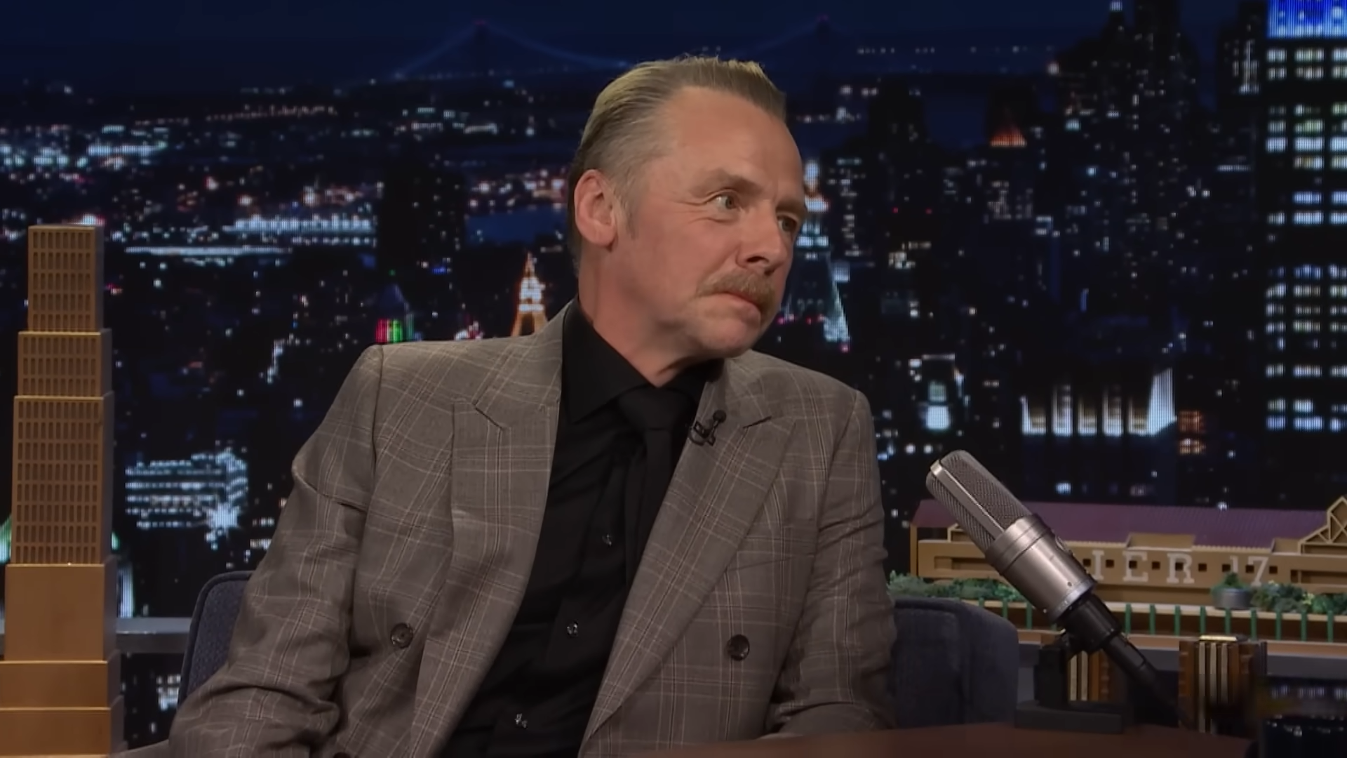 A man on a late-night show leans toward the host, listening intently