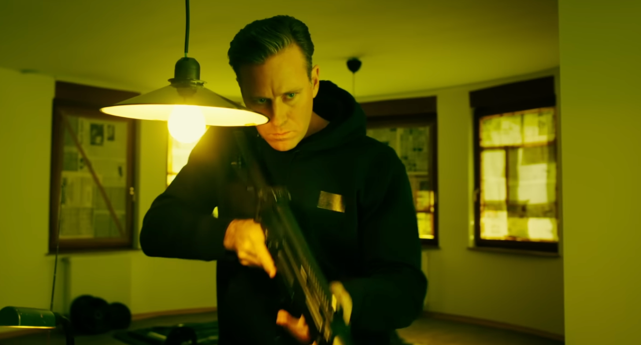 A man stands in a living room, holding a rifle