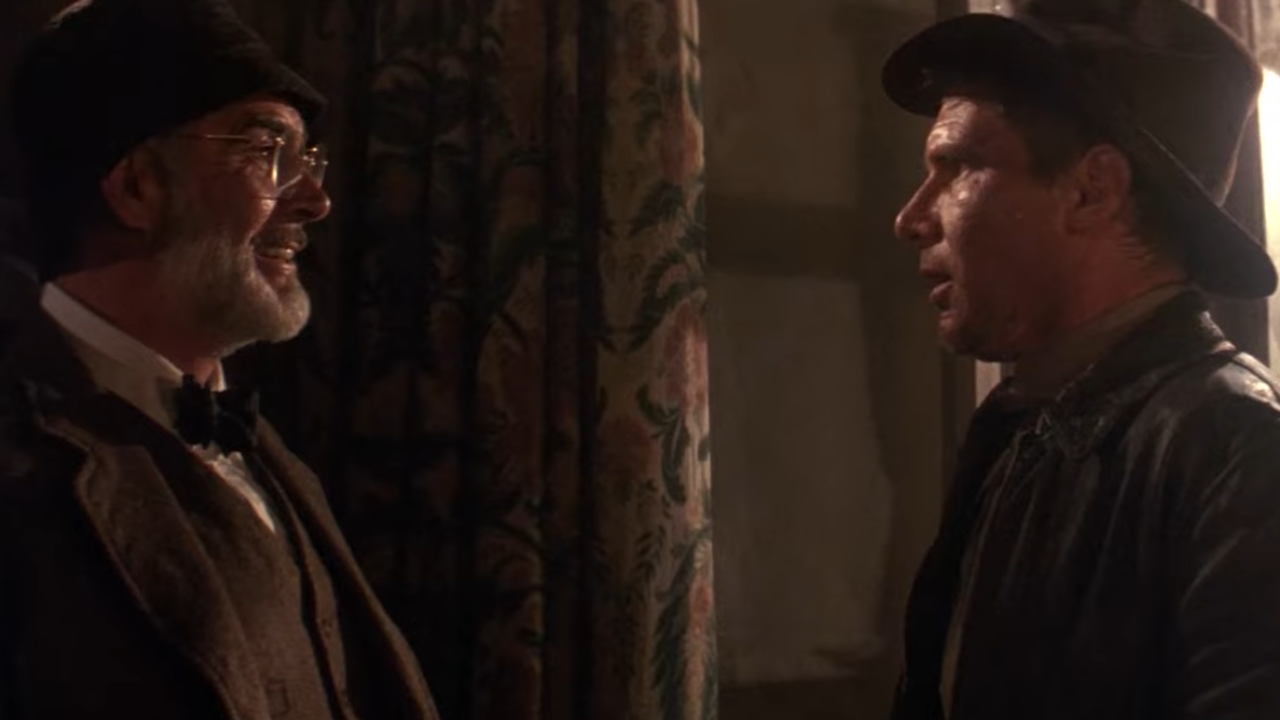 An older man smiling at a younger man, both in adventure attire
