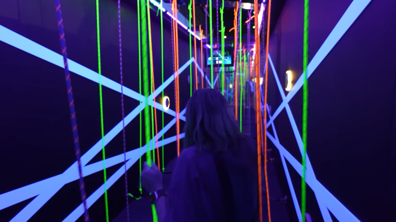 Woman navigating challenge with glow-in-the-dark floor-to-ceiling ropes