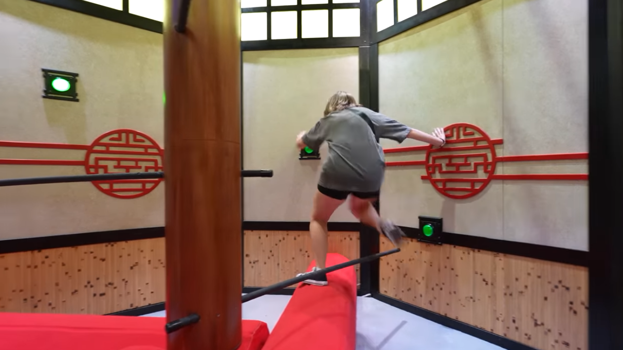 Woman climbing beams at varying lengths and angles to reach buttons to press to complete the challenge