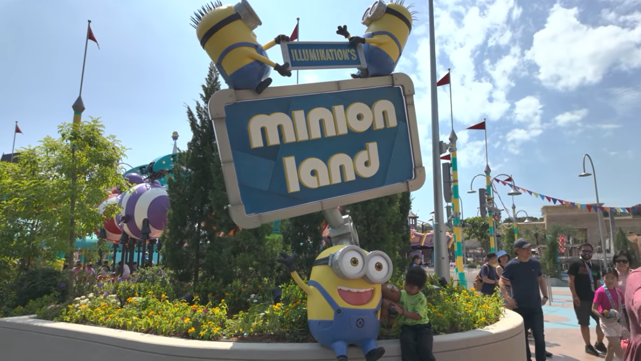Sign for Minion Land with two Minions atop and a boy posing next to a minion statue below