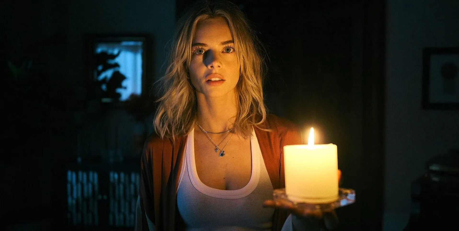 A young woman holds a candle, looking slightly afraid